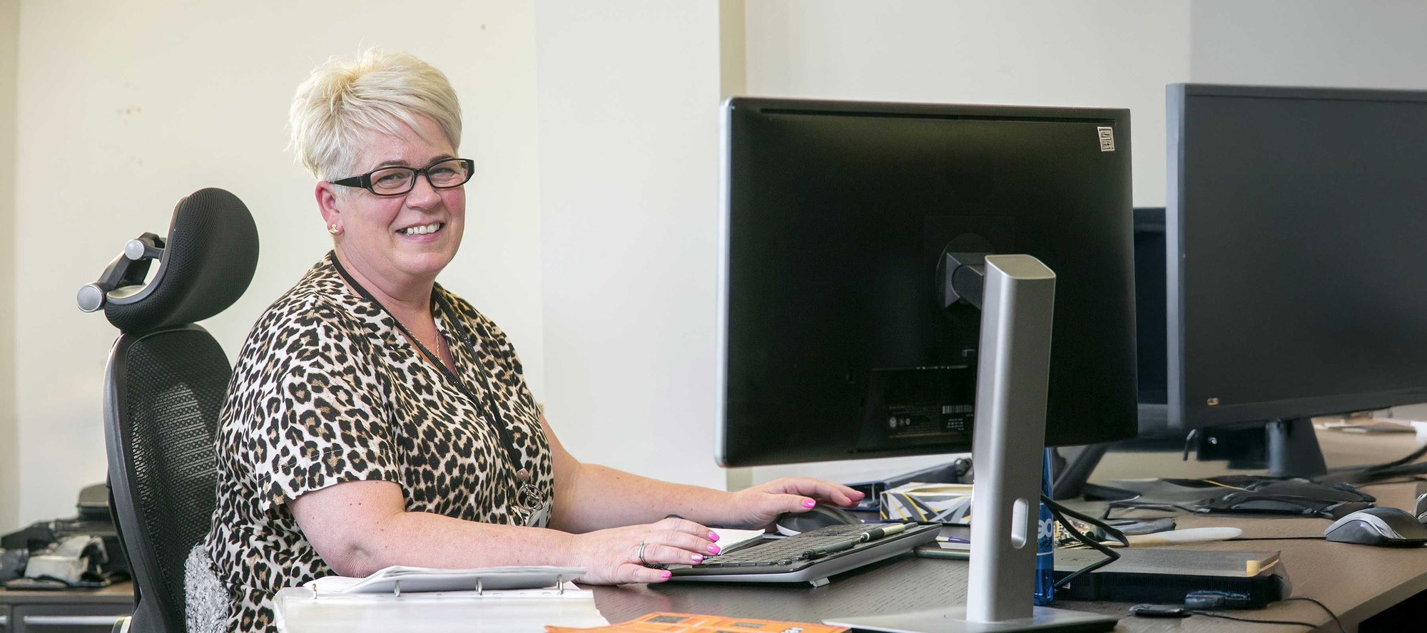 OEG certification administration assistant smiling at her desk.