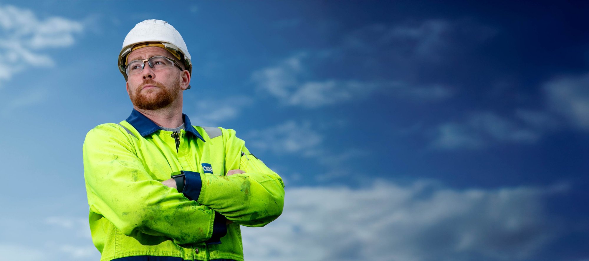 OEG worker with arms folded in front of blue sky.